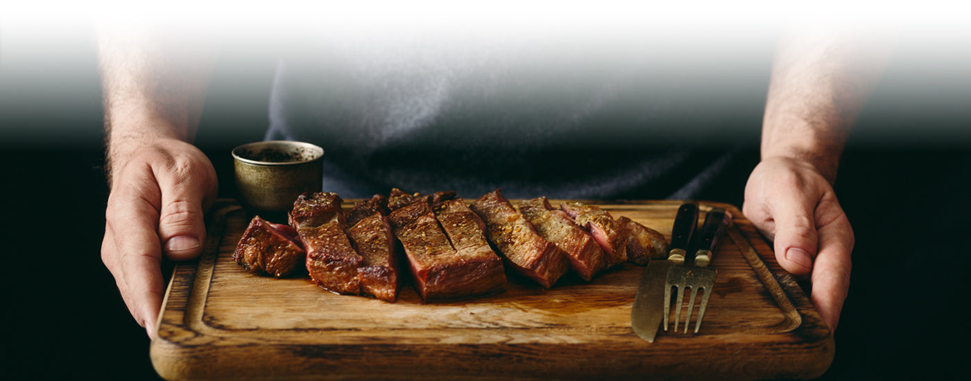 Man holding cutting board with grilled meat.